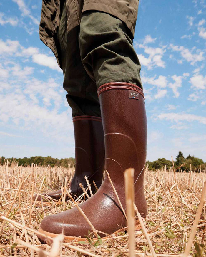 Maroon coloured Aigle Mens Tancar Pro Kevlar Reinforced Wellingtons on grassy background #colour_maroon