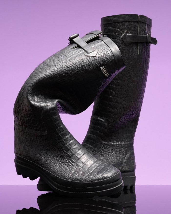 Noir coloured Aigle Womens Aiglentine 2 Crocodile Style Wellingtons on lilac background #colour_noir