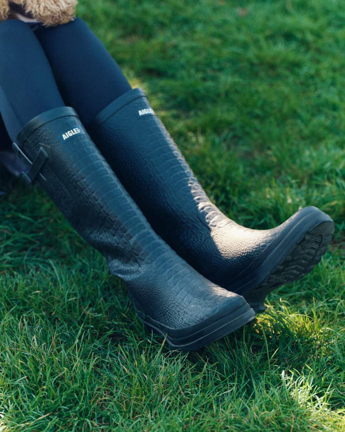 Noir coloured Aigle Womens Aiglentine 2 Crocodile Style Wellingtons on grass background #colour_noir