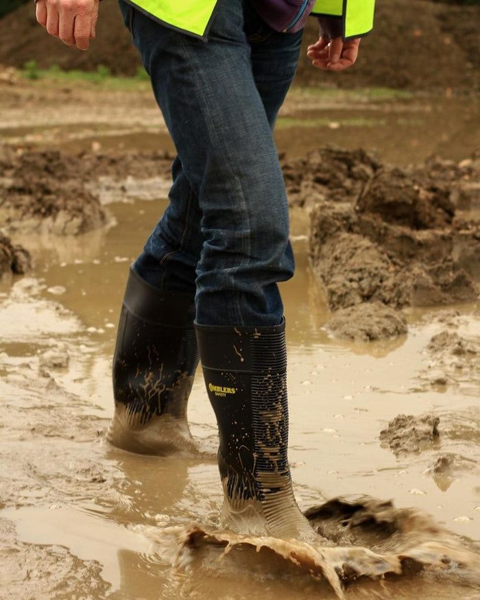 Black Coloured Amblers Safety FS100 Construction Safety Wellington on a muddy background #colour_black