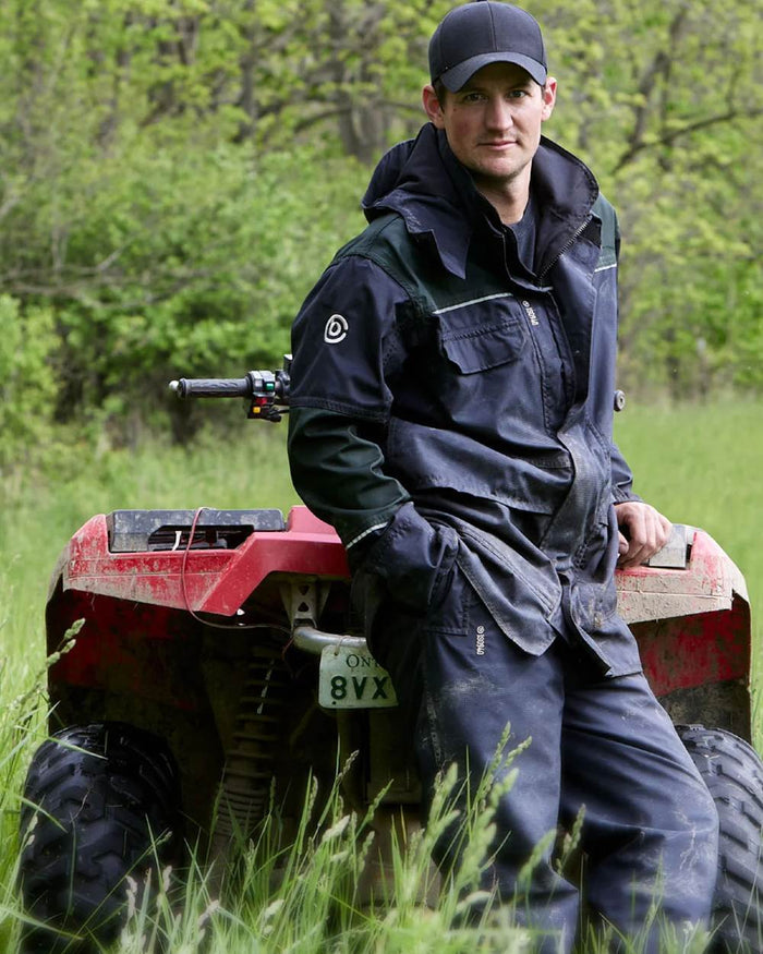 Black Moss Coloured Betacraft ISO940 Eco Over Trouser on forest background #colour_black-moss