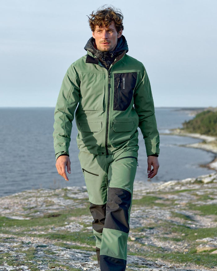 Dark Moss coloured Didriksons Mens Fractus Pants on sea background #colour_dark-moss