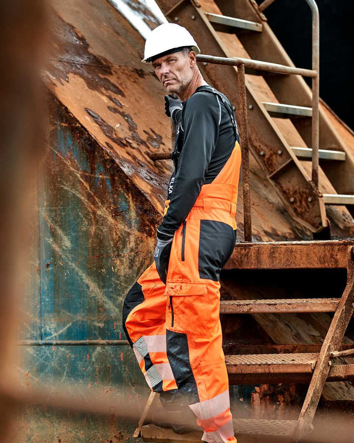 Fluorescent Orange Black Coloured Elka Mens Visible Xtreme Stretch Combi Trousers on construction background #colour_fluorescent-orange-black