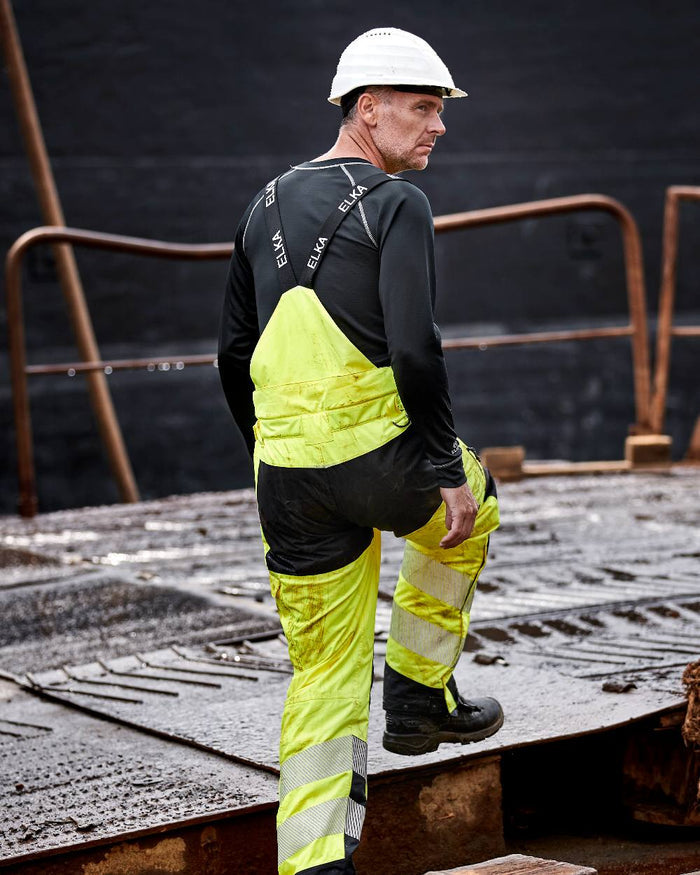 Fluorescent Yellow Black Coloured Elka Mens Visible Xtreme Stretch Combi Trousers on construction background #colour_fluorescent-yellow-black