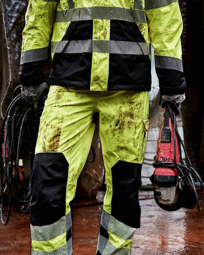Fluorescent Yellow Black Coloured Elka Mens Visible Xtreme Stretch Waist Trousers on construction background #colour_fluorescent-yellow-black