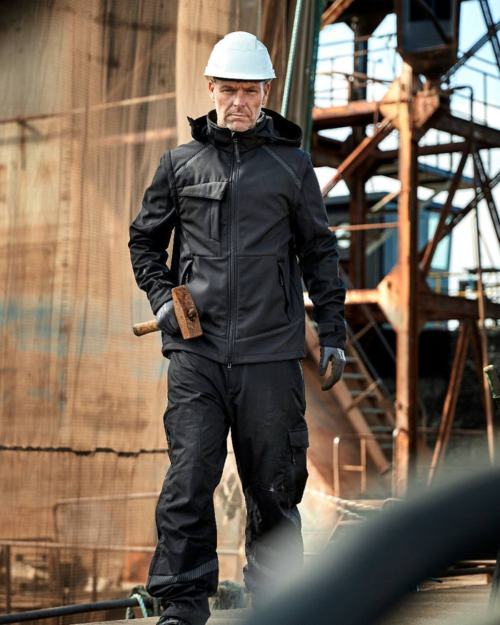 Black Coloured Elka Mens Working Xtreme Softshell Jacket With Detachable Sleeves on construction background #colour_black