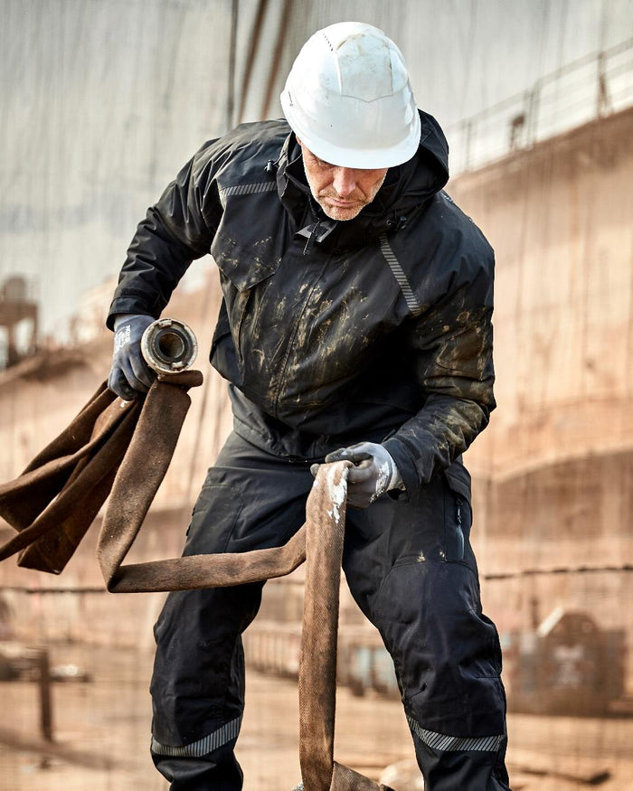 Black Coloured Elka Mens Working Xtreme Stretch Waist Trousers on construction background #colour_black
