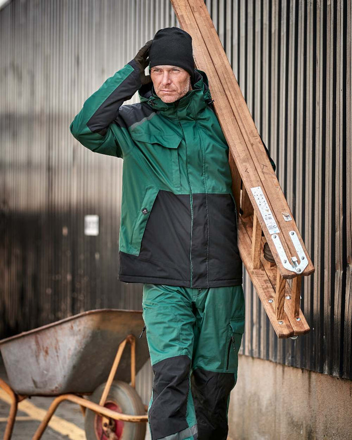 Green Black Coloured Elka Mens Working Xtreme Stretch Waist Trousers on construction background #colour_green-black