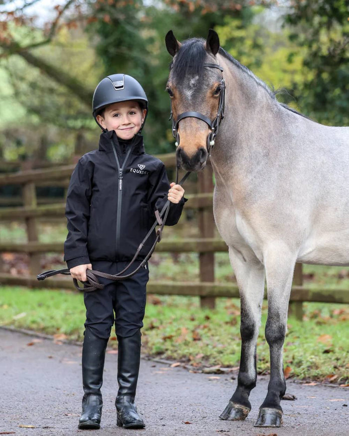 Black coloured Equidry Childrens Nimbus Pack Away Jacket With Stowaway Hood on outdoor background #colour_black