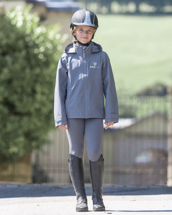 Charcoal coloured Equidry Childrens Nimbus Pack Away Jacket With Stowaway Hood on outdoor background #colour_charcoal