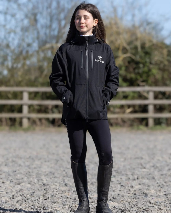 Black coloured Equidry Childrens Varsha Waterproof Jacket on farm background #colour_black