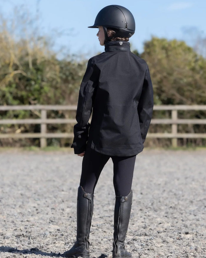 Black coloured Equidry Childrens Varsha Waterproof Jacket on farm background #colour_black