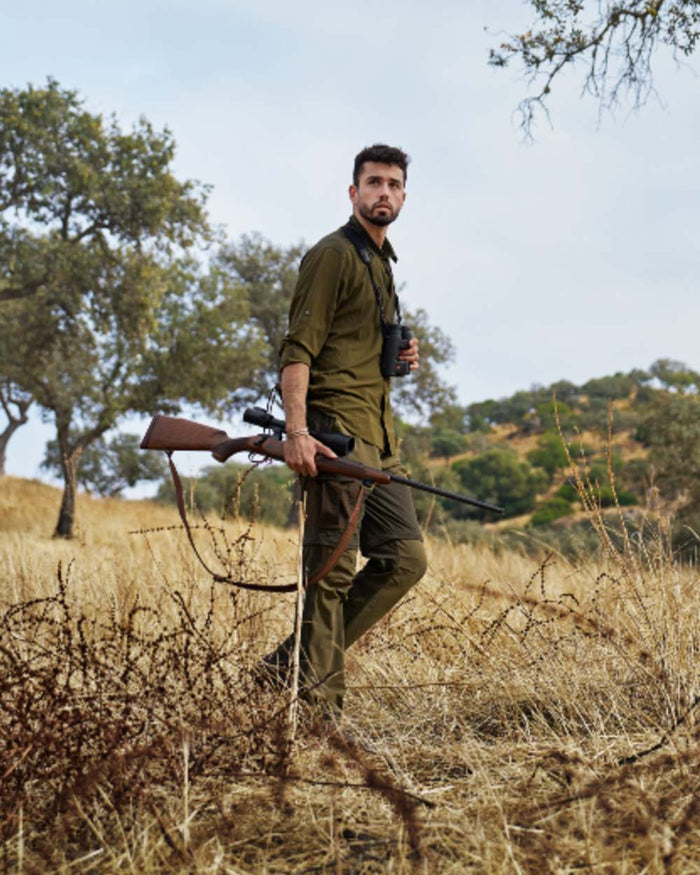 Dark Olive Willow Green Coloured Harkila Logmar Lightweight Zip Off Trousers on forest background #colour_dark-olive-willow-green