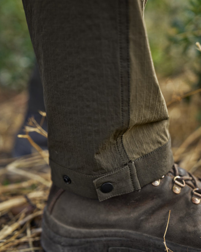Dark Olive Willow Green Coloured Harkila Logmar Lightweight Zip Off Trousers on forest background #colour_dark-olive-willow-green