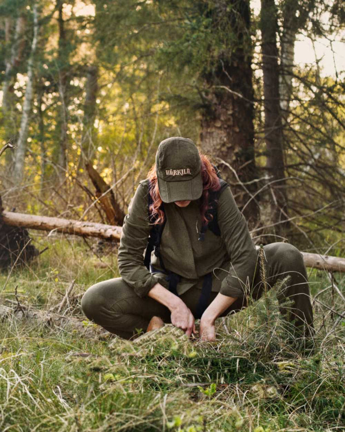 Willow Green Coloured Harkila Womens Herlet Tech Shirt on forest background #colour_willow-green