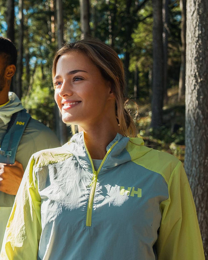 Sharp Green coloured Helly Hansen Womens Roam Wind Anorak on forest background #colour_sharp-green