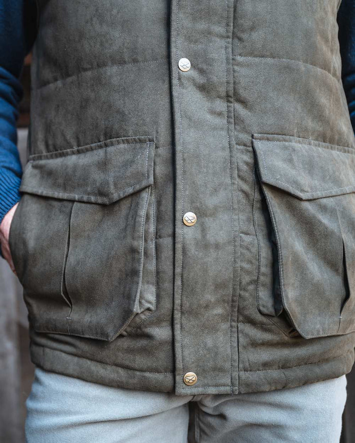 Loden coloured Hoggs of Fife Mens Glenbervie Quilted Gilet on blurry background #colour_loden