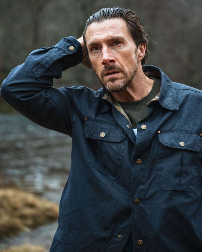 Midnight Navy Coloured Hoggs of Fife Mens Huntly Waxed Canvas Utility Overshirt on blurry background #colour_midnight-navy