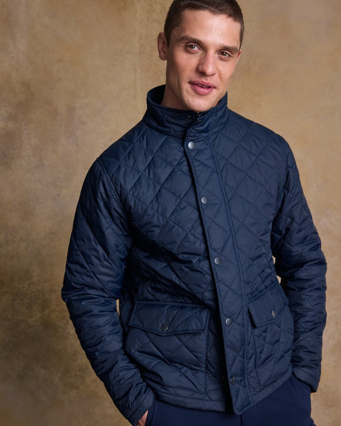 Navy coloured Jack Murphy Ronan Quilted Jacket on wall background #colour_navy