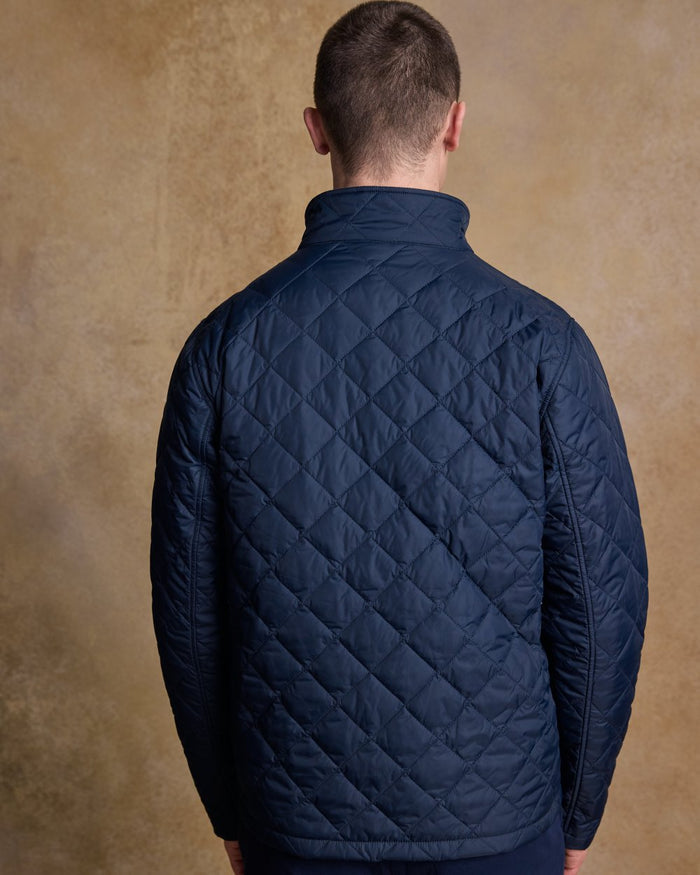 Navy coloured Jack Murphy Ronan Quilted Jacket on wall background #colour_navy