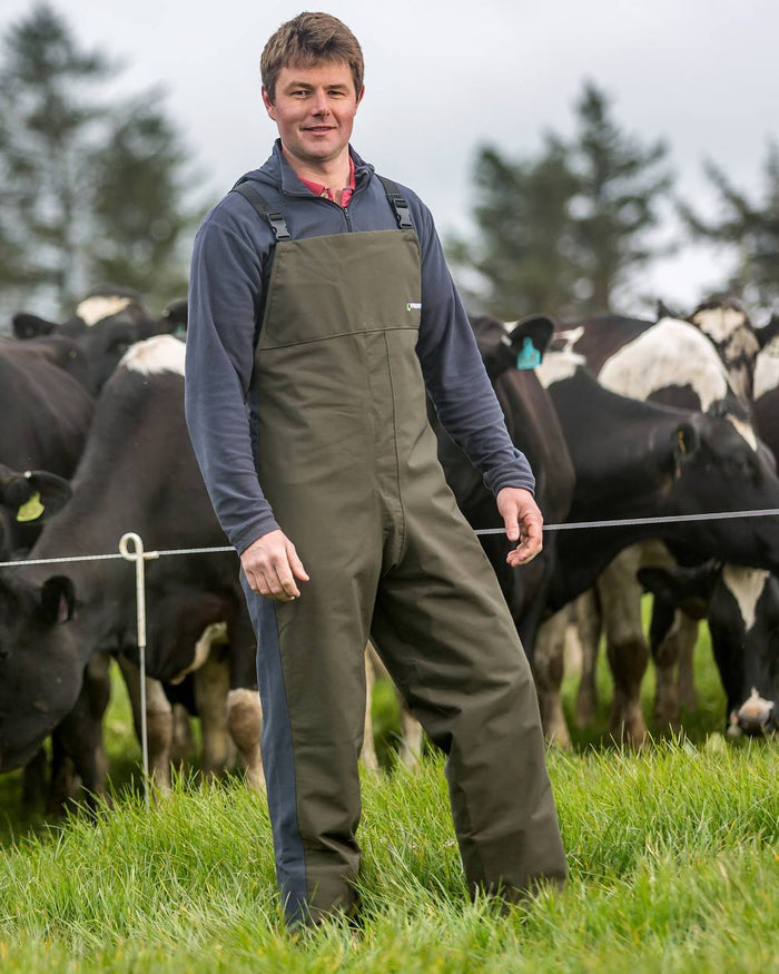 Olive coloured Kaiwaka Mens Stormforce Bib Overtrousers on farm background #colour_olive