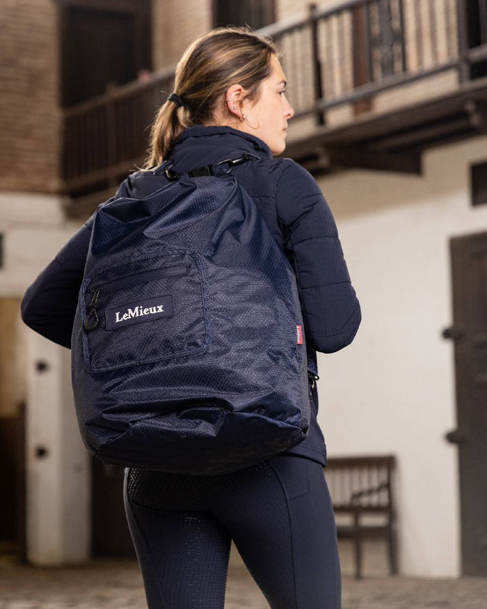 Navy coloured LeMieux Carry All Backpack with blurry building in background #colour_navy