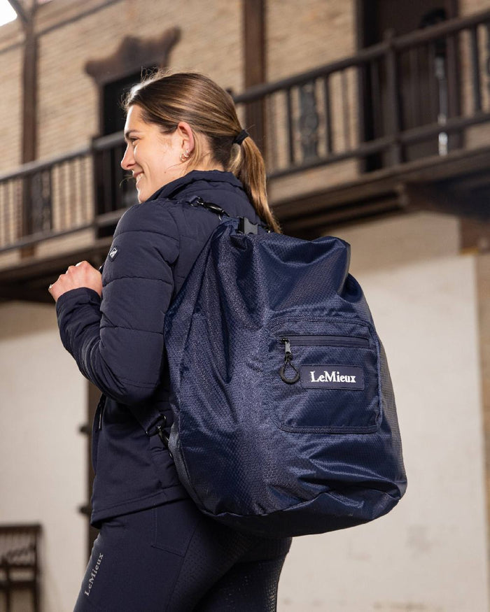 Navy coloured LeMieux Carry All Backpack with blurry building in background #colour_navy