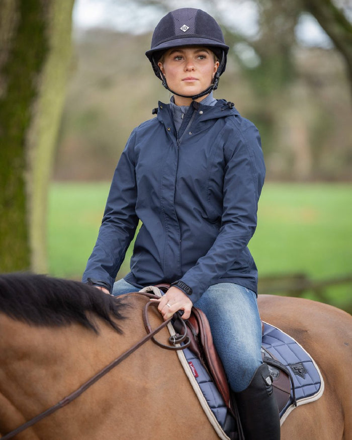 Navy coloured LeMieux Isla Short Waterproof Jacket on blurry background #colour_navy
