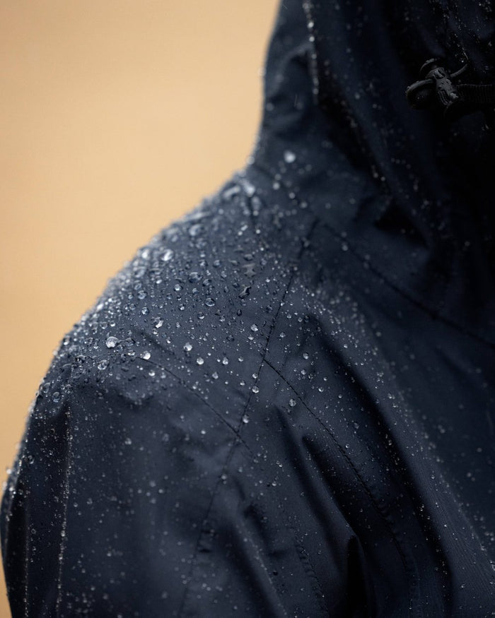 Navy coloured LeMieux Isla Short Waterproof Jacket on brown background #colour_navy