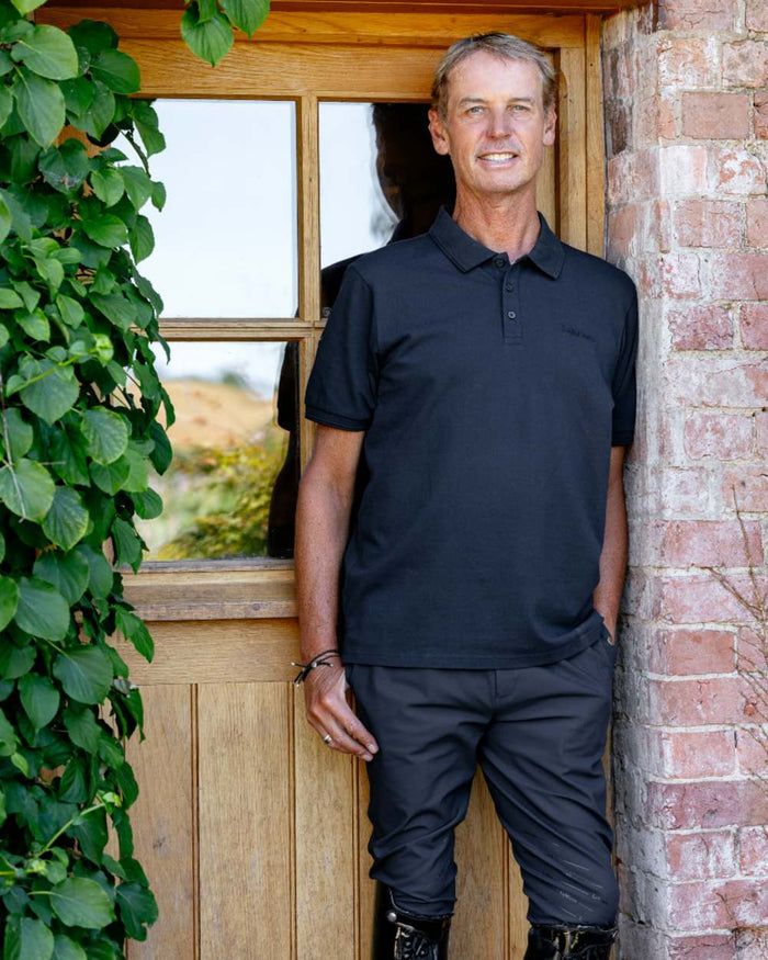 Black coloured LeMieux Mens Classique Polo T-Shirt on outdoor background #colour_black