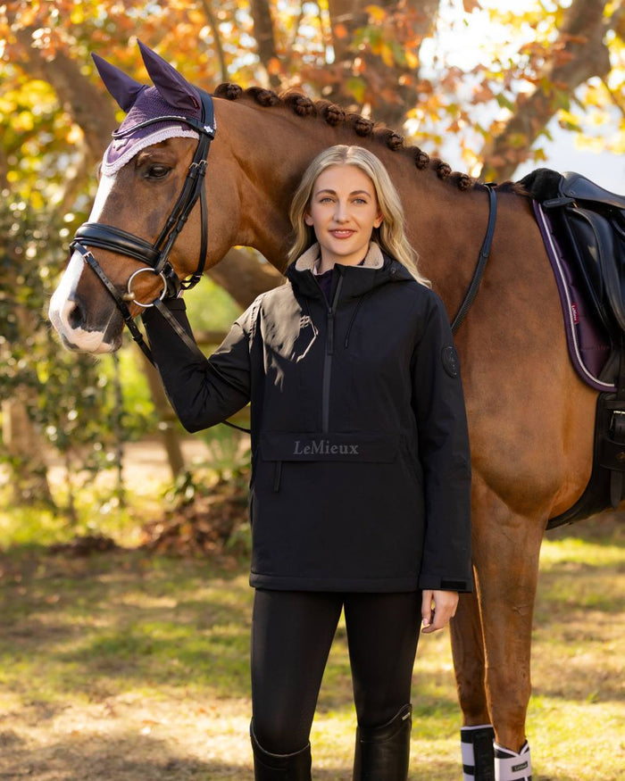 Black coloured LeMieux Phoebe Half Zip Waterproof Anorak on tree background #colour_black