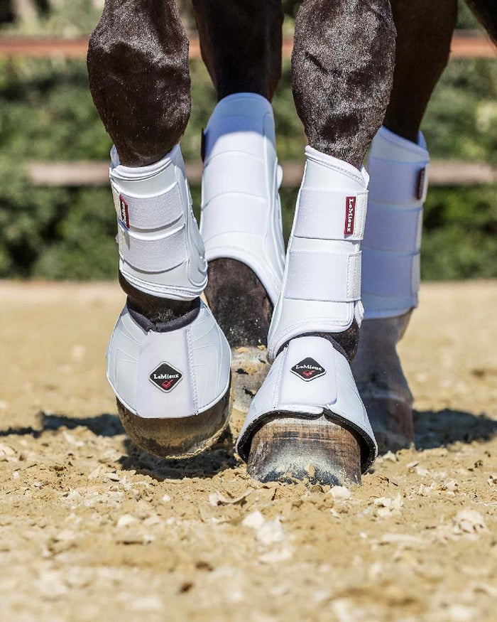 White coloured LeMieux ProShell Over Reach Boots on blurry background #colour_white