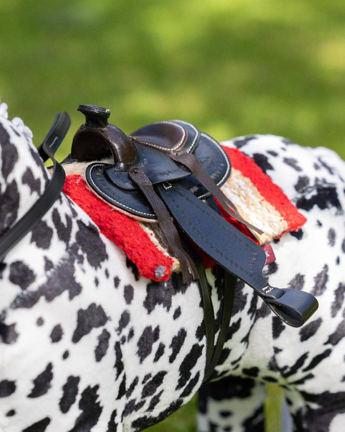 Black coloured LeMieux Toy Pony Western Saddle on blurry green background #colour_black