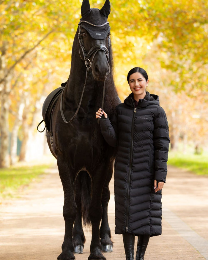 Black coloured LeMieux Womens Hayley Water Resistant Longline Puffer Coat on tree background #colour_black