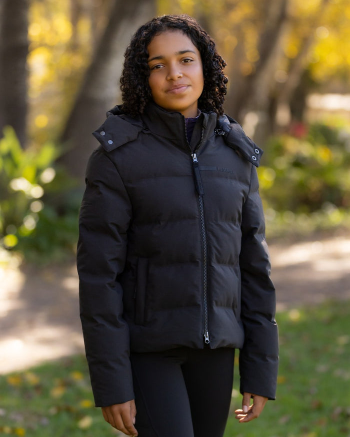 Black coloured LeMieux Young Rider Daisy Waterproof Coat on garden background #colour_black