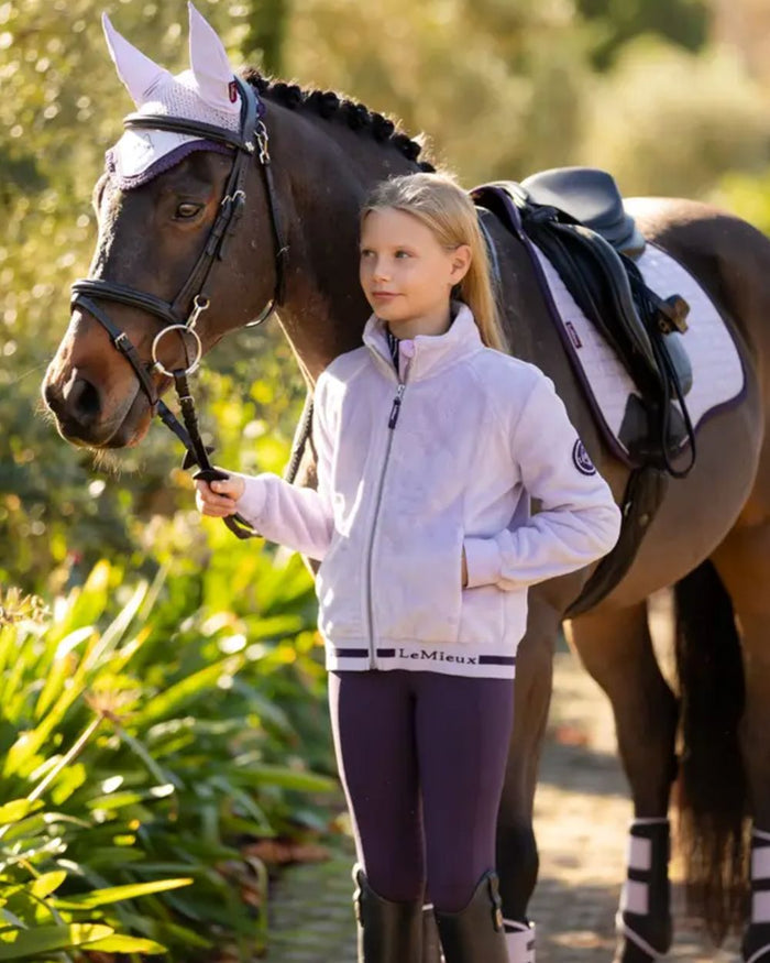 Lilac Coloured LeMieux Young Rider Libby Fleece Jacket On A Leafy Background #colour_lilac