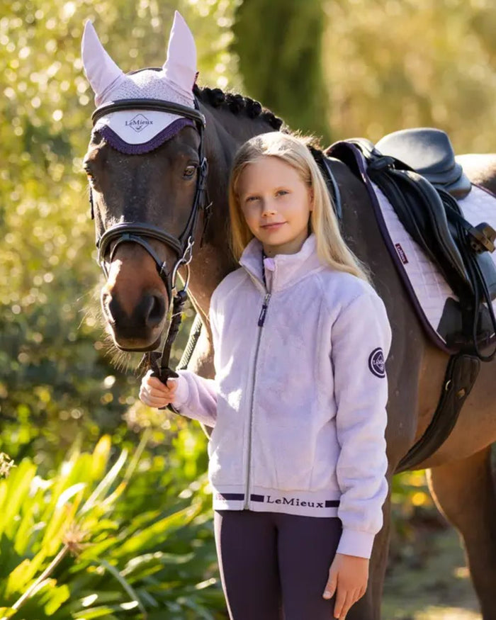 Lilac Coloured LeMieux Young Rider Libby Fleece Jacket On A Leafy Background #colour_lilac