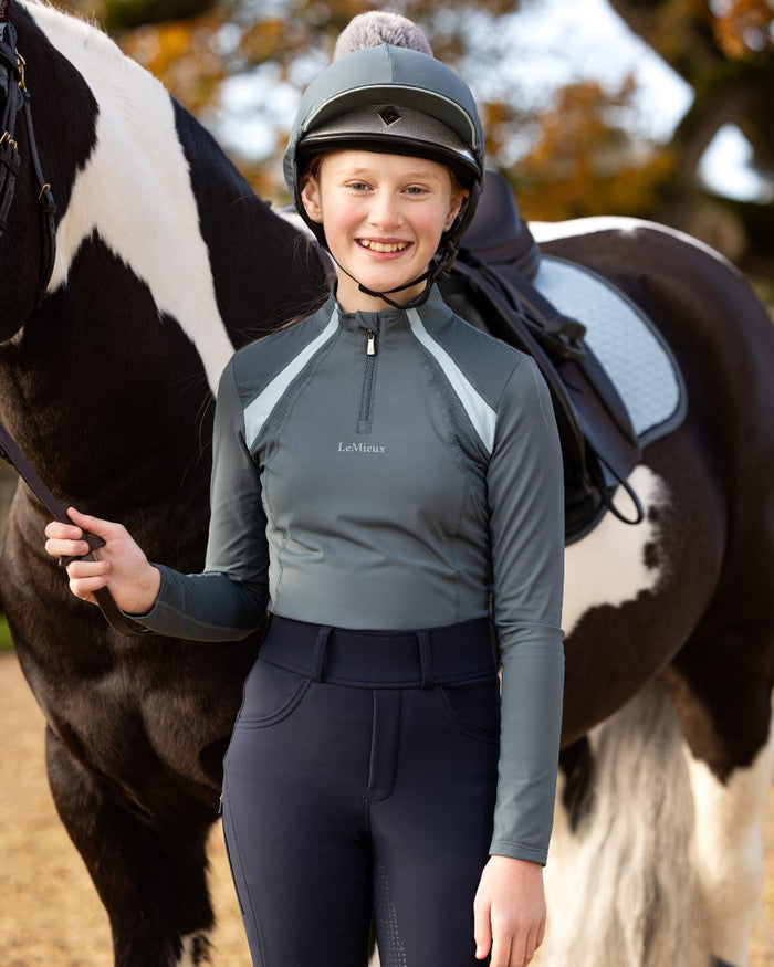 Petrol Coloured LeMieux Young Rider Mia Mesh Base Layer On A  Blurry Background #colour_petrol