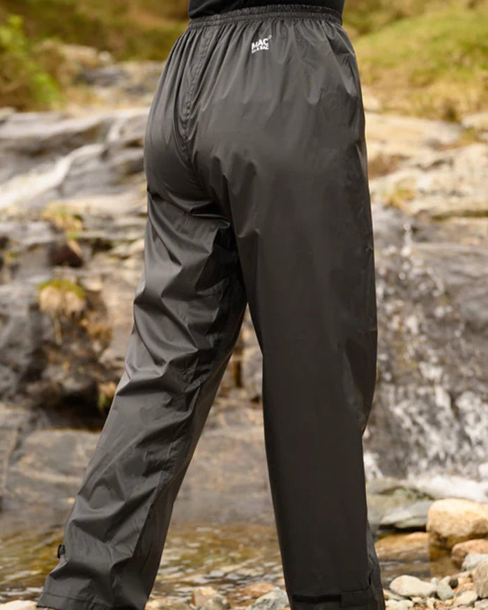 Black coloured Mac In A Sac Origin Packable Waterproof Overtrousers on blurry background #colour_black