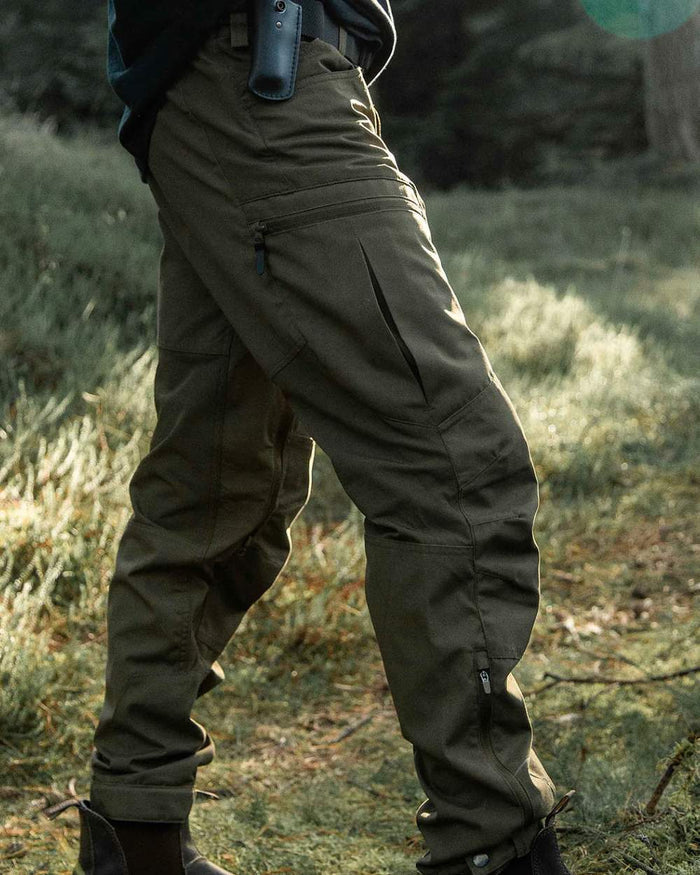 Olive coloured Northern Hunting Mens Trond Pro Outdoor Trousers on forest background #colour_olive
