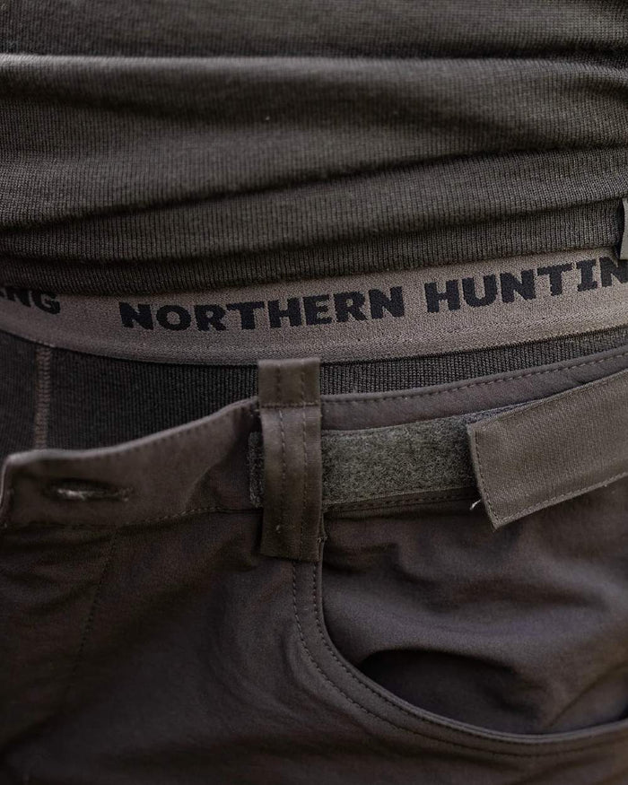 Dark Green coloured Northern Hunting Norr Fal Baselayer Pants on forest background #colour_dark-green