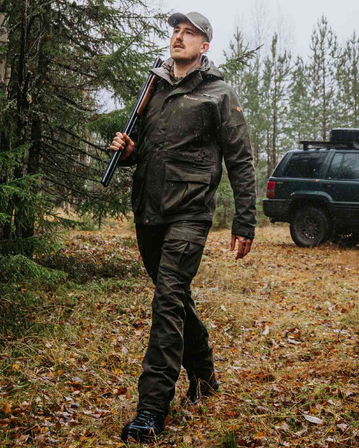 Dark Moss Green coloured Pinewood Mens Furudal Expert 2L Hunting Jacket on forest background #colour_dark-moss-green