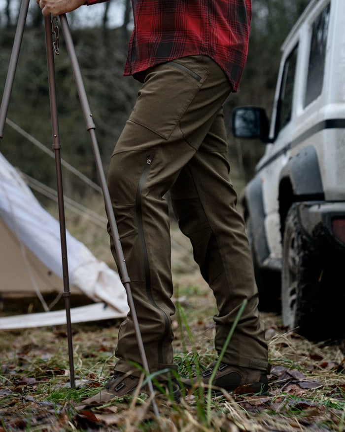 Pine Green Grizzly Brown coloured Seeland Mens Spruce Membrane Trousers on forest background #colour_pine-green-grizzly-brown