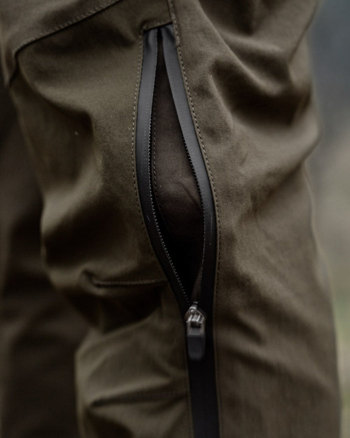 Pine Green Grizzly Brown coloured Seeland Mens Spruce Membrane Trousers on forest background #colour_pine-green-grizzly-brown