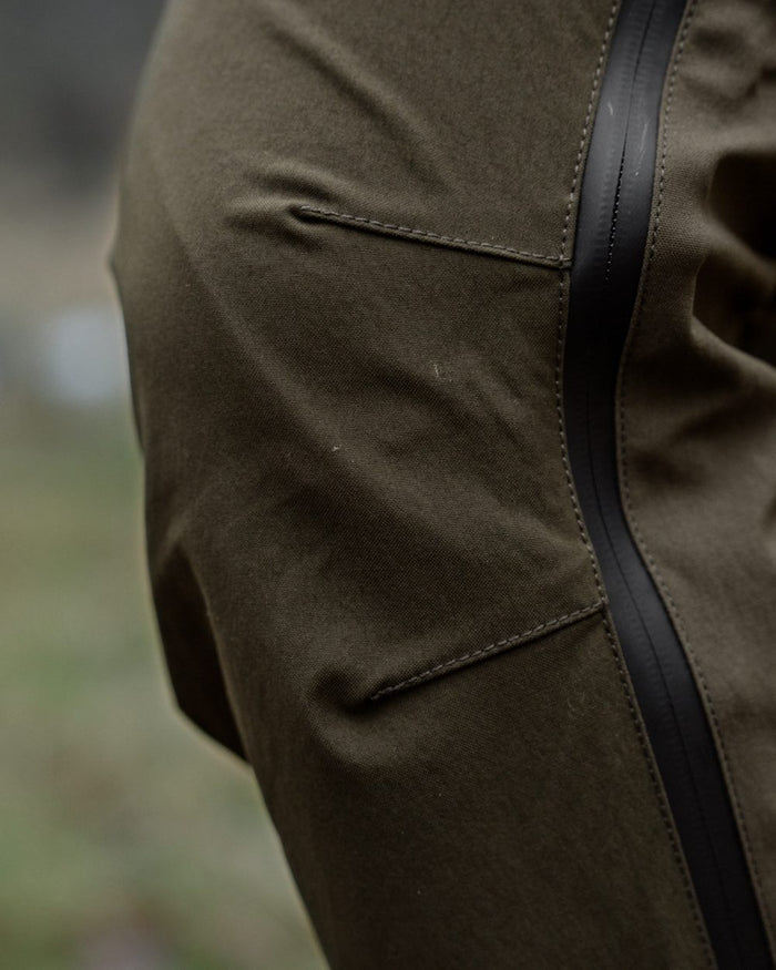 Pine Green Grizzly Brown coloured Seeland Mens Spruce Membrane Trousers on forest background #colour_pine-green-grizzly-brown