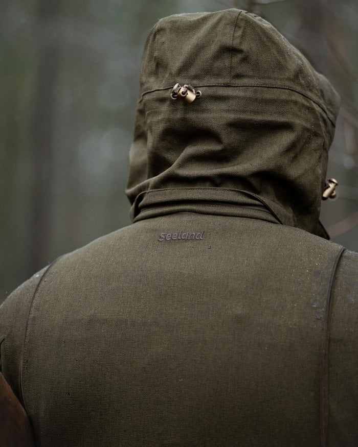 Shaded Olive coloured Seeland Mens Woodcock Royale Jacket on forest background #colour_shaded-olive