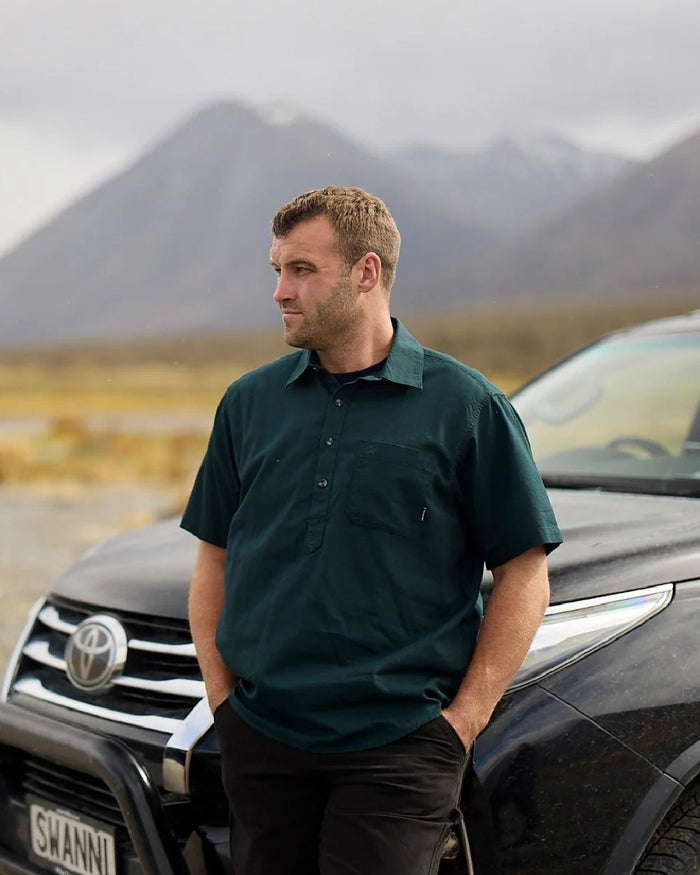 Forest Green Coloured Swanndri Mens Paihia Short Sleeve Shirt on mountain background #colour_forest-green