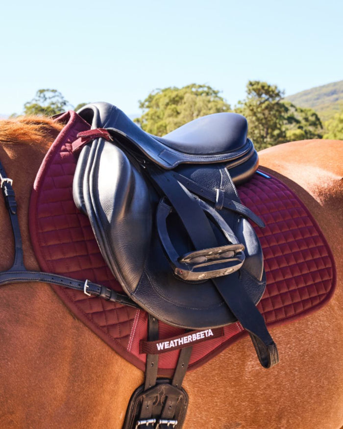 Burgundy Coloured WeatherBeeta Prime Air-Tec Jump Shaped Saddle Pad on horse background #colour_burgundy
